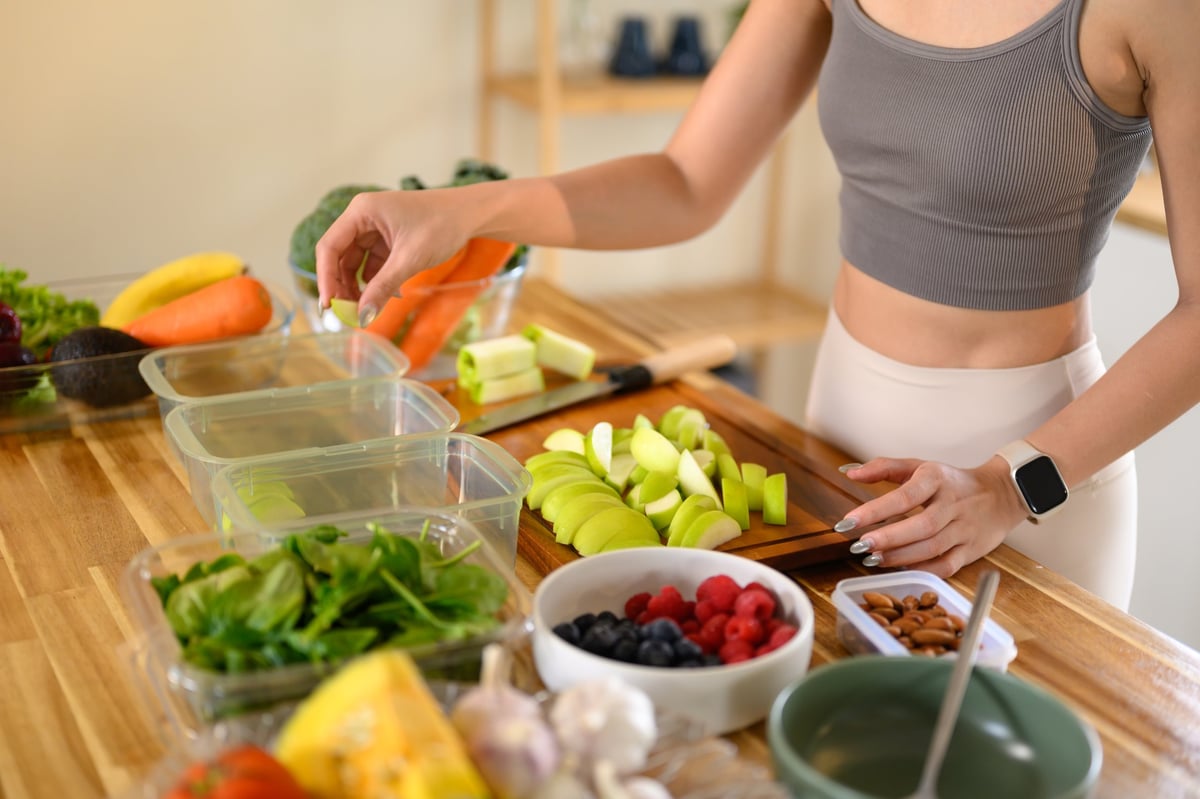 Closeup of a woman hand placing freshly cut fruits and vegetables into food storage containers, meal prep, and food preservation.